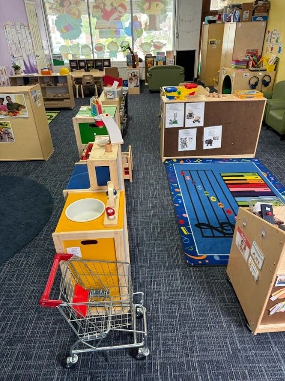 Organized classroom with play kitchen, shopping cart, and interactive learning stations