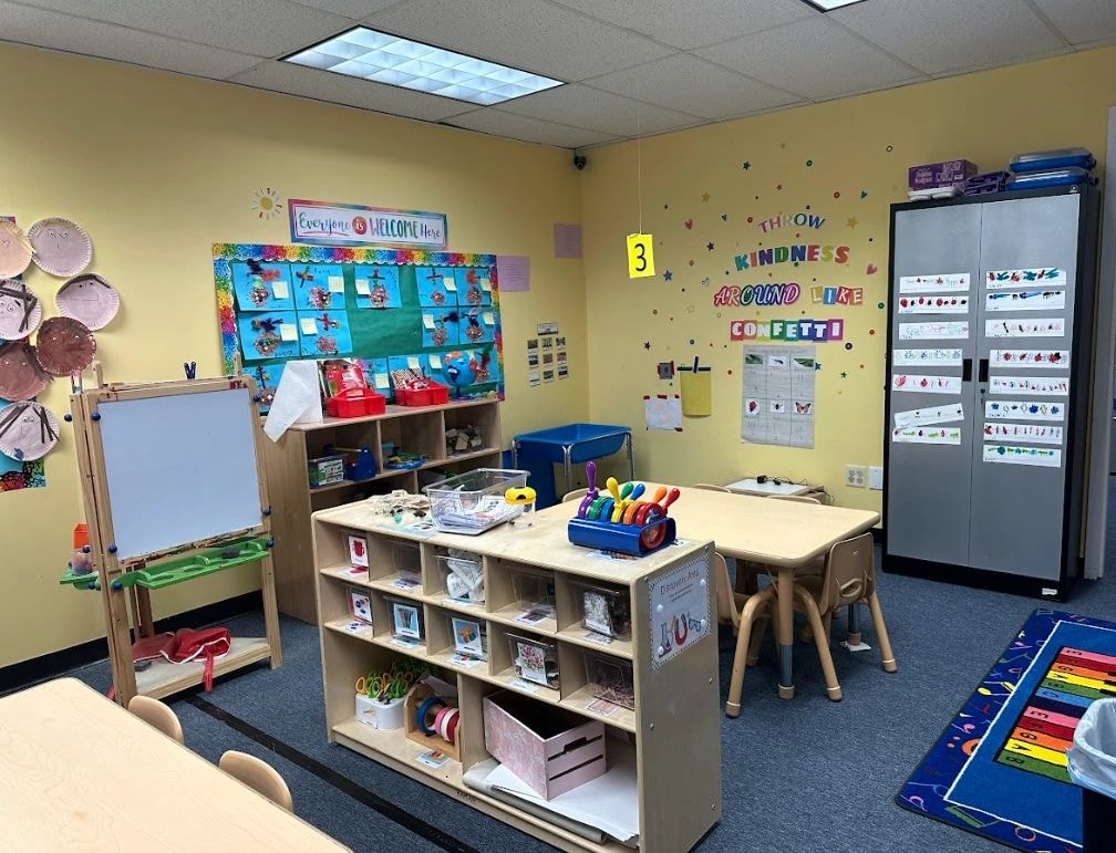 Yellow-walled classroom with educational posters, shelving units, and learning workstations